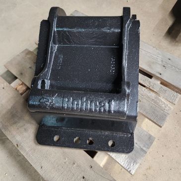 Metal Bobcat machine part on a wooden pallet.