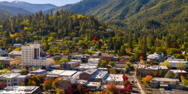 A small town nestled in a valley with colorful autumn trees and surrounding forested mountains.