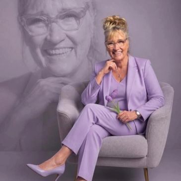 Elegant elderly woman in lavender suit sitting with a flower.