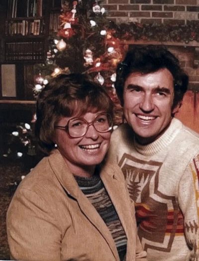 Smiling couple by a Christmas tree and fireplace.