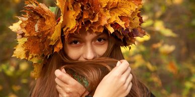 Woman wearing a crown of autumn leaves, holding her hair near her face.