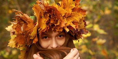 Woman wearing a crown of autumn leaves, holding her hair near her face.
