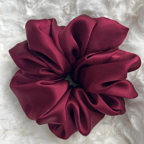 A large, silky maroon scrunchie on a white fluffy surface.