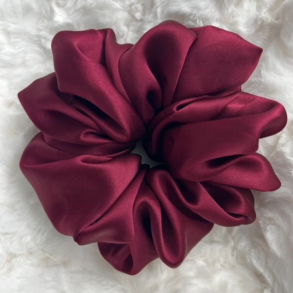 A large, burgundy satin scrunchie on a white fluffy surface.