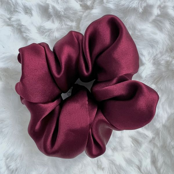 A shiny maroon satin scrunchie on a fluffy white surface.