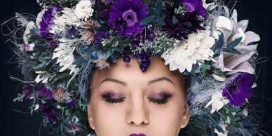 Woman with eyes closed wearing a vibrant floral crown with purple and white flowers.