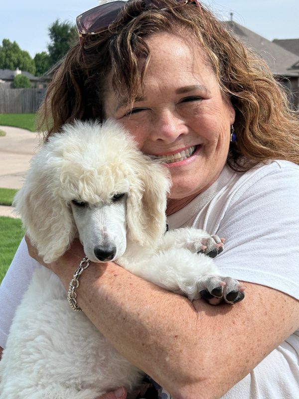Woman smiling and hugging a fluffy white poodle puppy outdoors.
