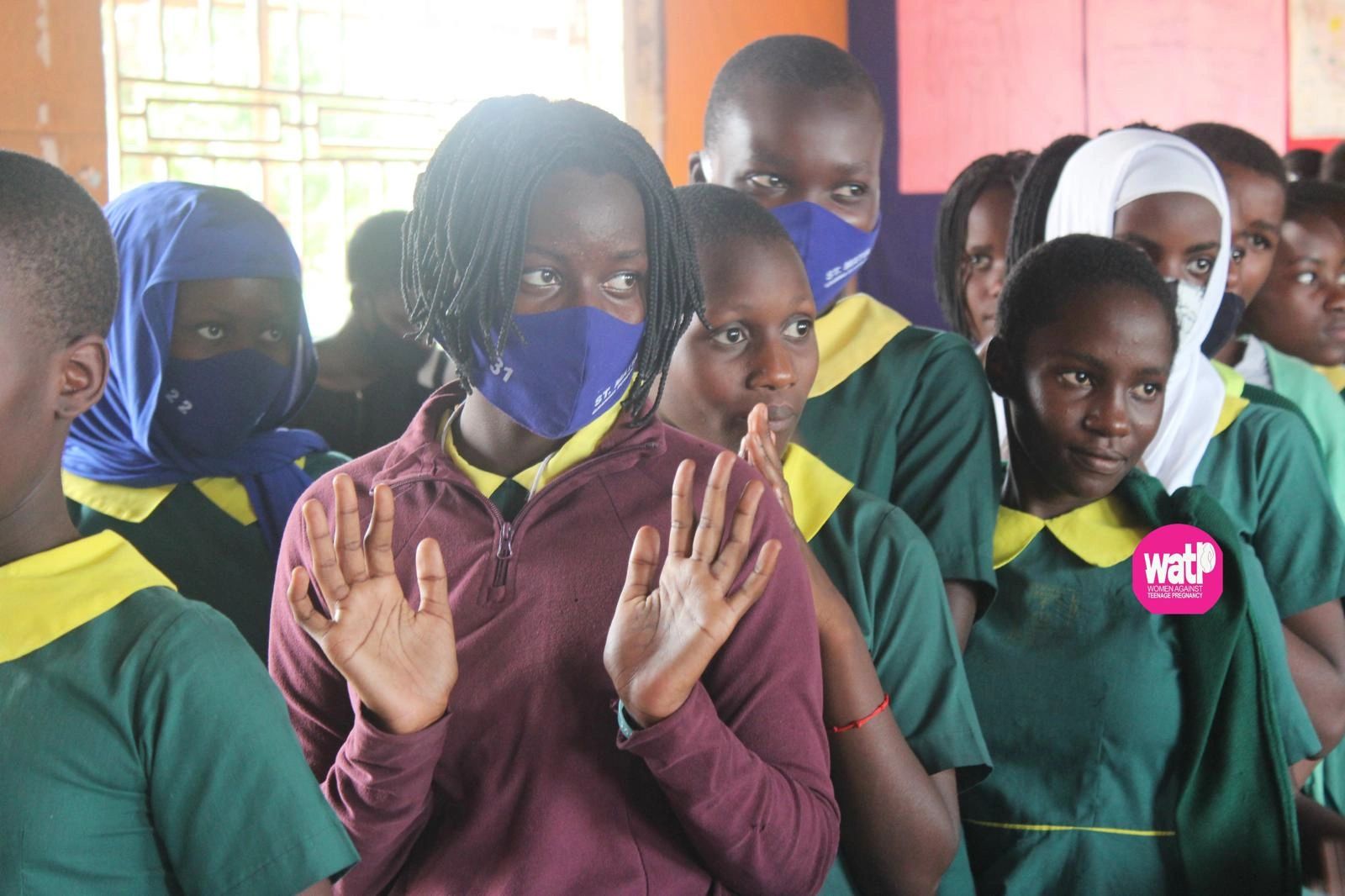 Students in green uniforms, some wearing masks, attentively participate in a classroom setting.