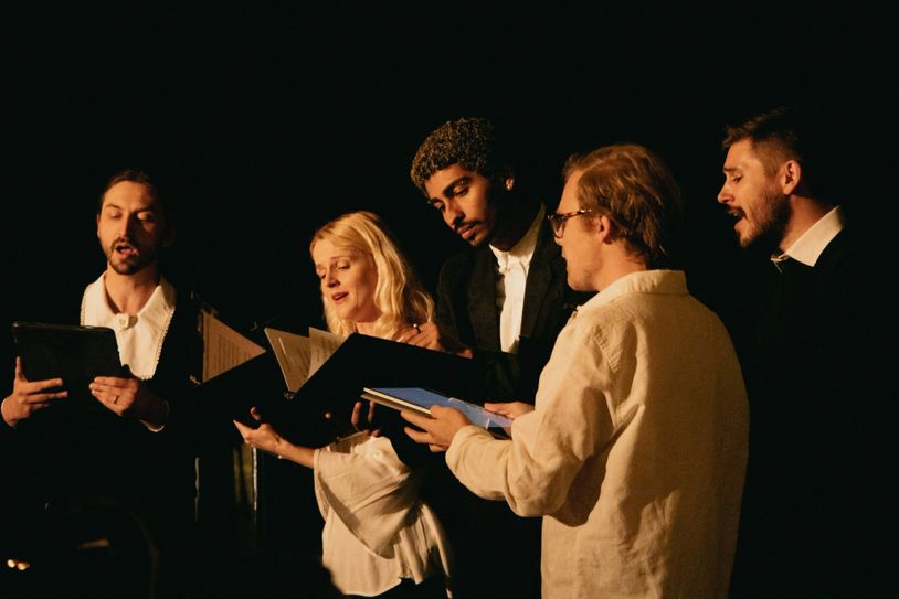 Group of five singers holding folders, performing in dim light.