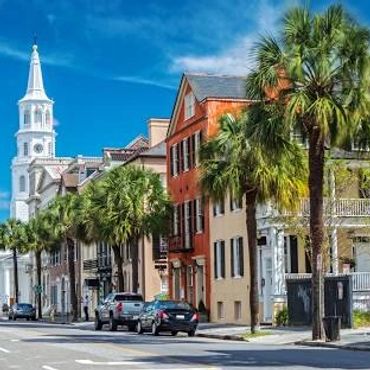 Historic street with palm trees and a white church steeple under a blue sky.