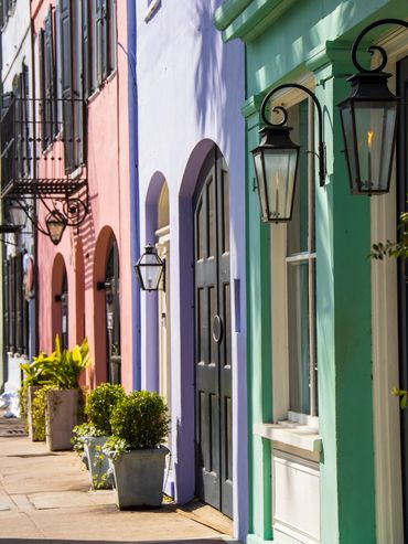 Colorful row houses with lanterns and lush greenery along a sunny sidewalk.