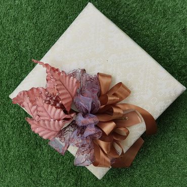 Elegant gift wrapped in cream paper with brown and purple ribbons on green grass.