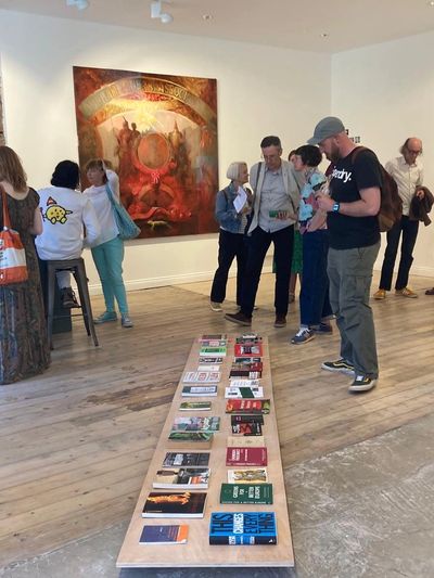 Visitors to our members' show "Agree/Disagree". There is a painting on the wall, books on the floor.