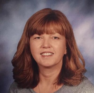 Portrait of a smiling woman with medium-length brown hair against a blue background.