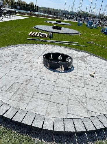 Outdoor fire pits with decorative metal rings on stone patios in a grassy area.