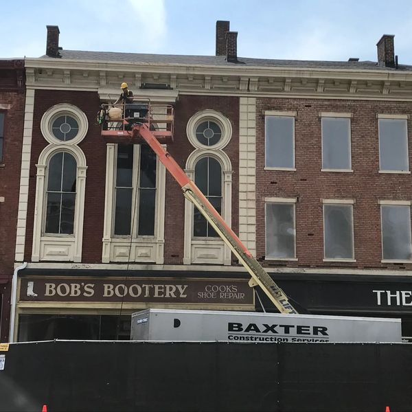 A construction worker is working on the side of a building on a bucket truck.  