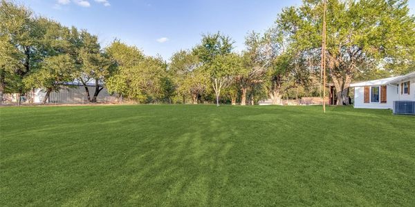 Spacious backyard with lush green grass and surrounding trees under a clear sky.