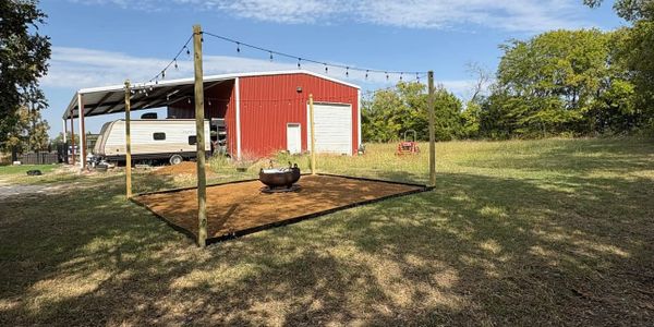 Outdoor fire pit area with string lights near a red barn and trailer.