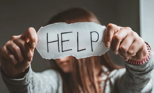 Person holding torn paper with 'HELP' written on it.