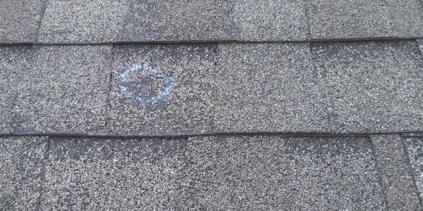 Roof shingles with a chalk-marked spot indicating damage.