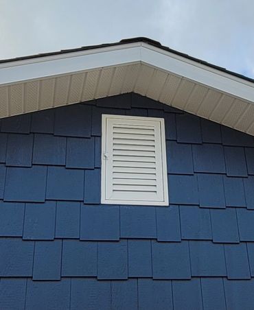 White vent on blue shingled house wall under roof peak.