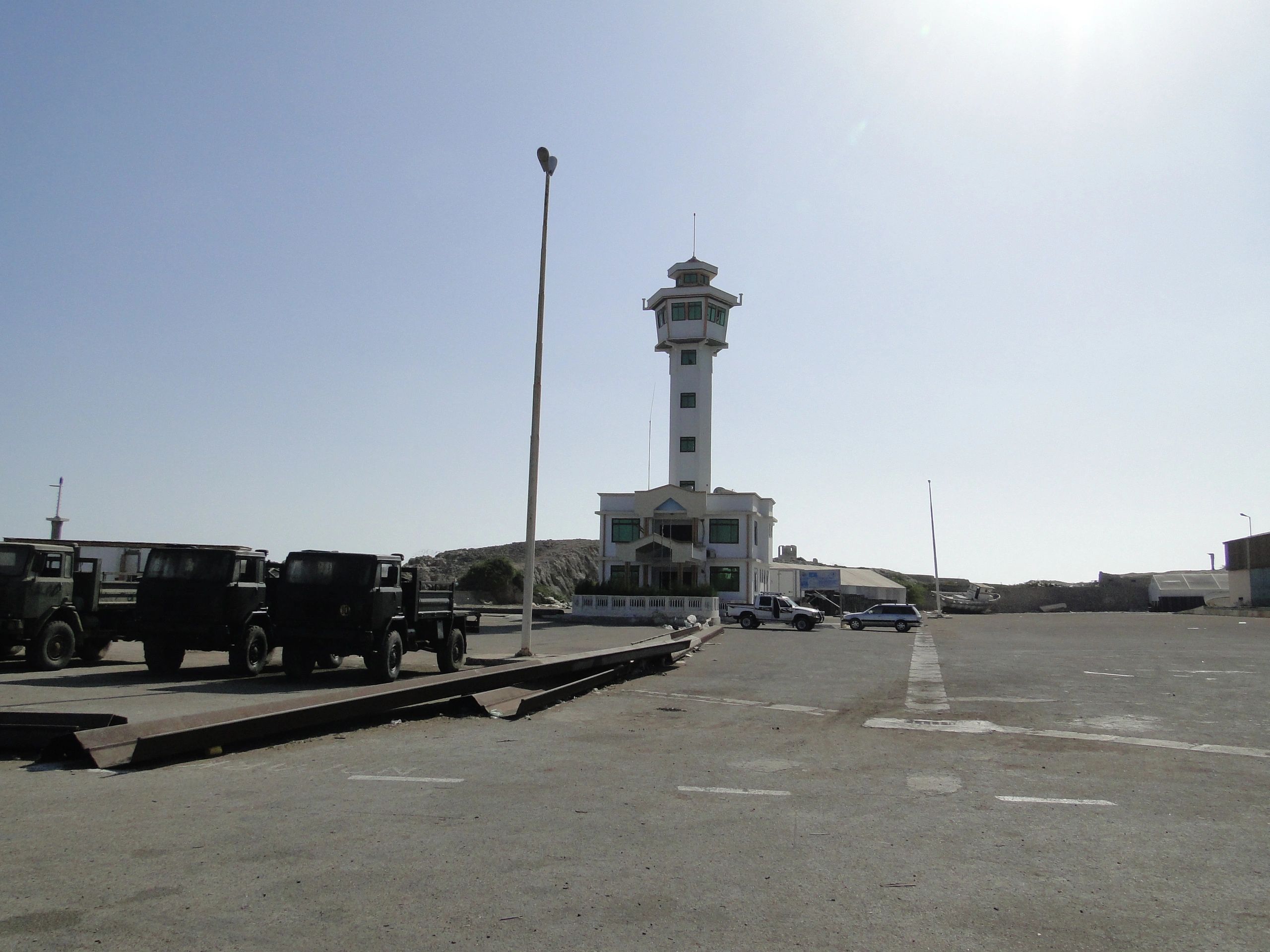 Control tower at a desolate airstrip with parked vehicles.