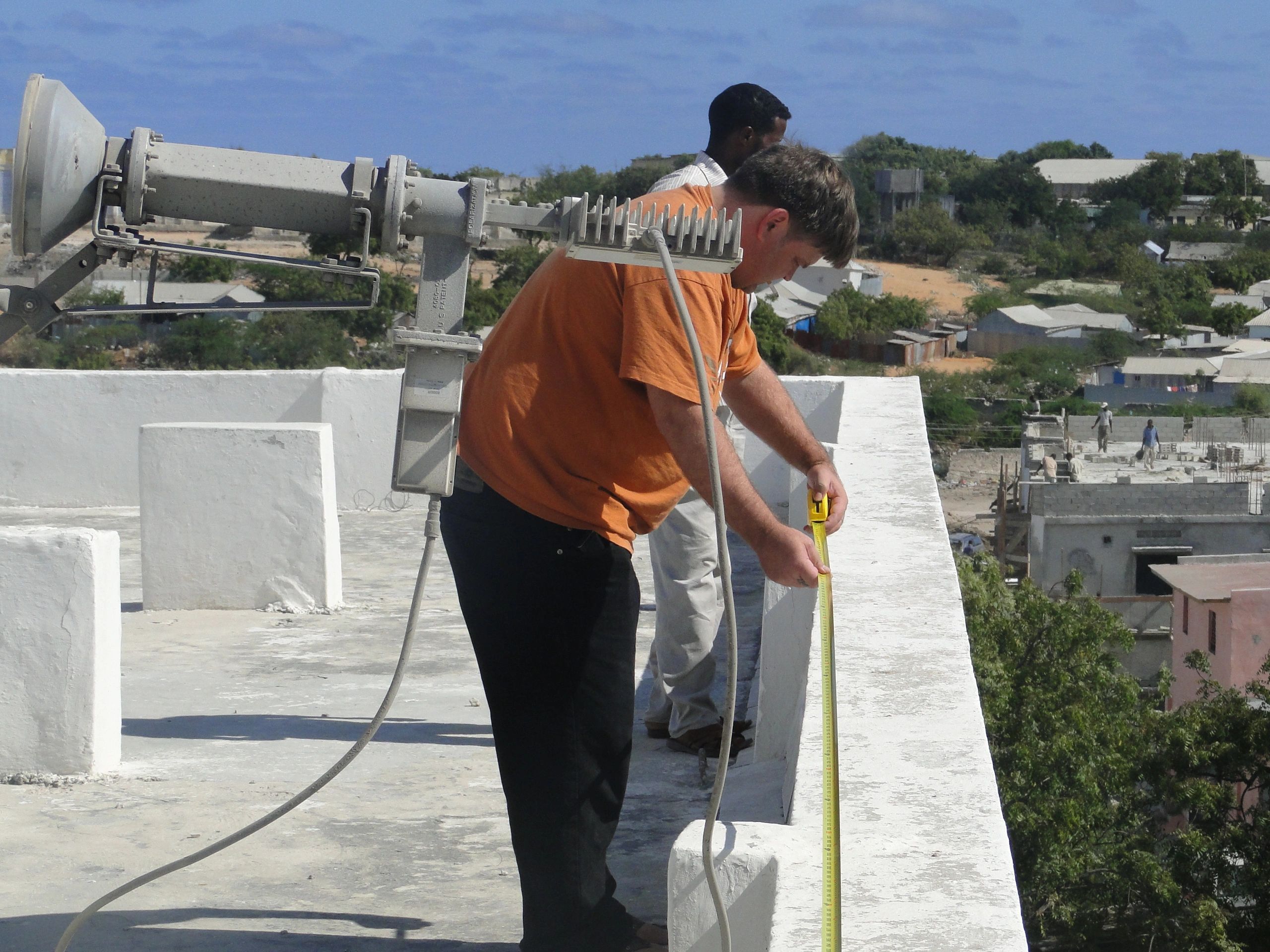 Two men measuring rooftop dimensions with a tape measure.