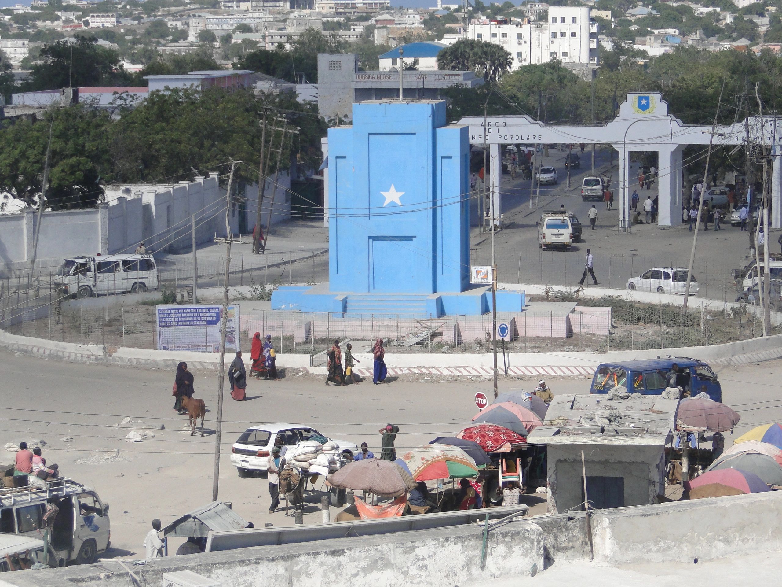 Busy urban area with a blue monument and people crossing street.