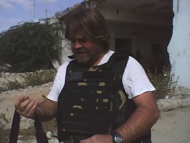 Man wearing camouflage tactical vest outdoors.