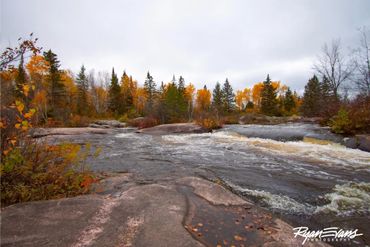 A flowing river surrounded by autumn trees and rocks under a cloudy sky.