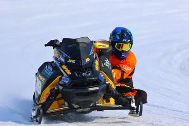 Snowmobile racer in orange gear speeding on snow.