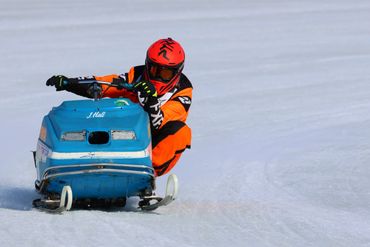 Person in orange racing a blue snowmobile on snow.