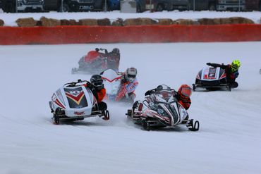 Four racers speeding on snowmobiles during a winter race.