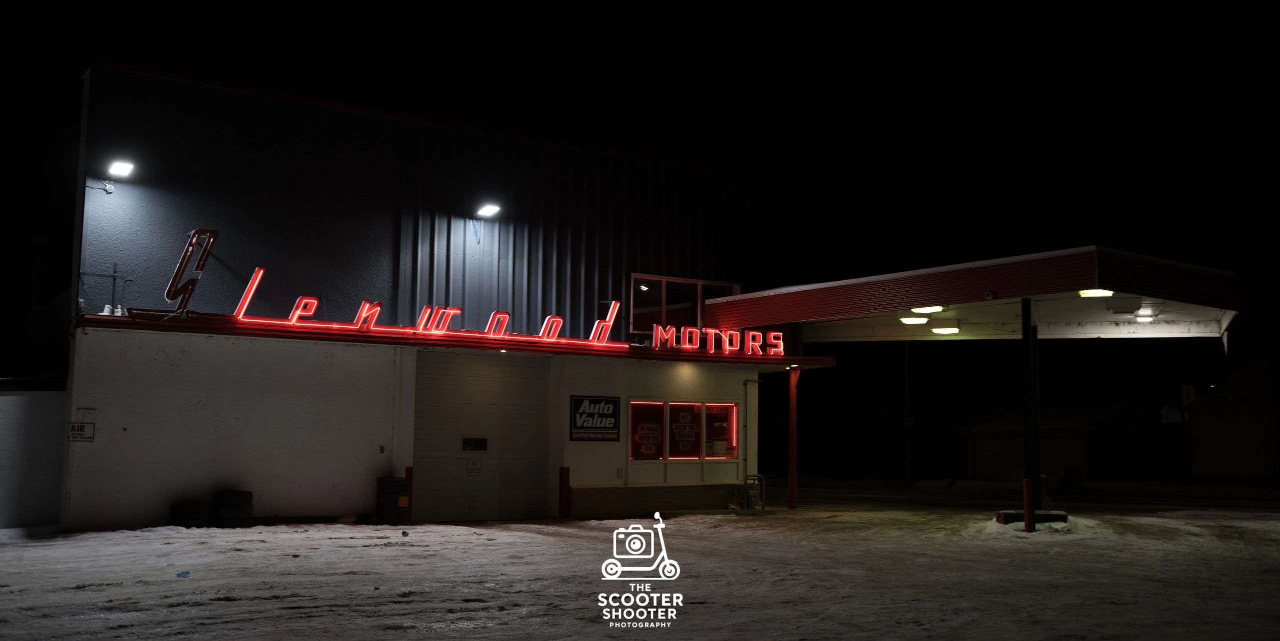 Red neon sign of Lenwood Motors illuminated at night on a snowy ground.