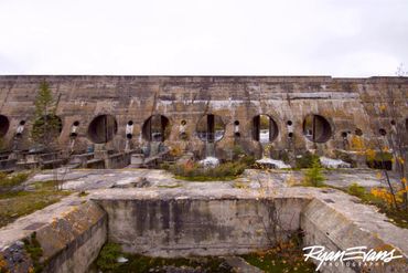 Abandoned concrete structure with circular openings and overgrown vegetation.