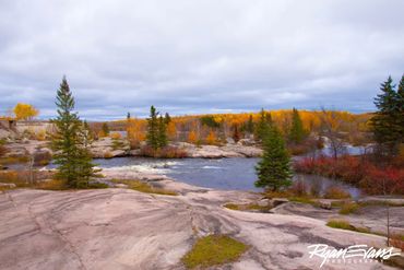 Rocky river landscape with autumn trees under a cloudy sky.