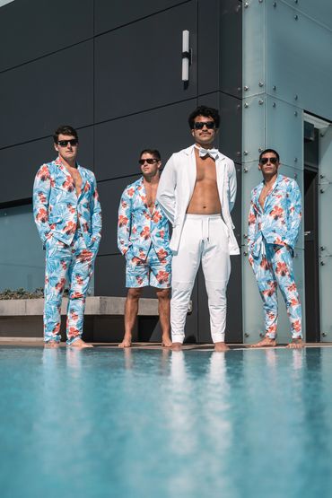 men in all white and hawaiian swim suits standing next to the pool 