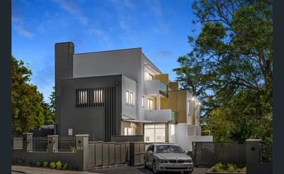 Modern multi-story house with a car parked in front under a blue evening sky.