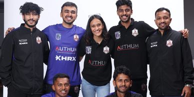 A cheerful group of seven young adults posing together in team apparel against a white backdrop.