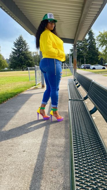 Woman in colorful heels and yellow jacket standing by a bench.