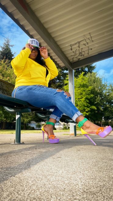Woman in colorful heels, yellow jacket, and cap.