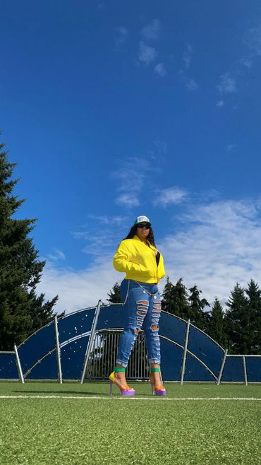 Woman in yellow jacket and ripped jeans on grass field.