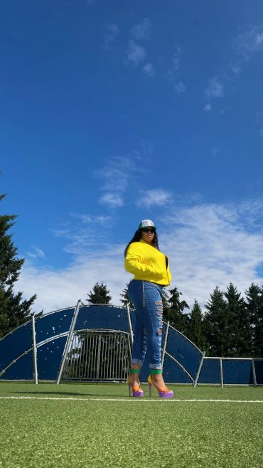 Woman in yellow jacket and ripped jeans on a field.