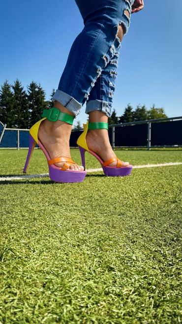Colorful high heels and ripped jeans on grass.