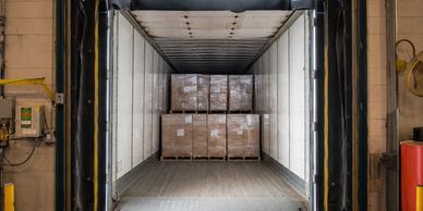 Pallets of goods loaded inside a shipping container in a warehouse.
