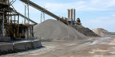 Industrial site with large gravel piles and conveyor belts under a blue sky.
