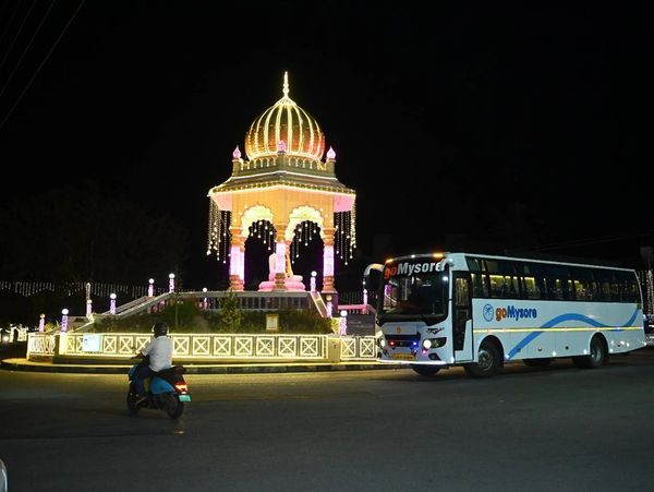 Illuminated monument and bus at night in Mysore city.