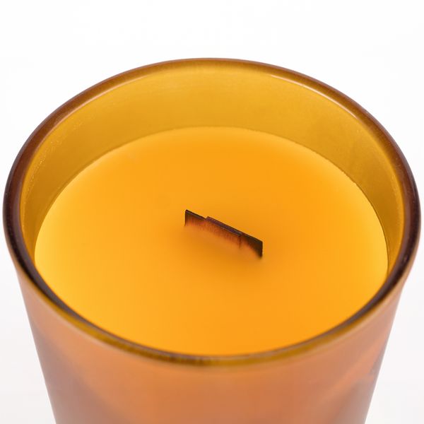 Close-up of an orange soy candle with a wooden wick in a glass holder.