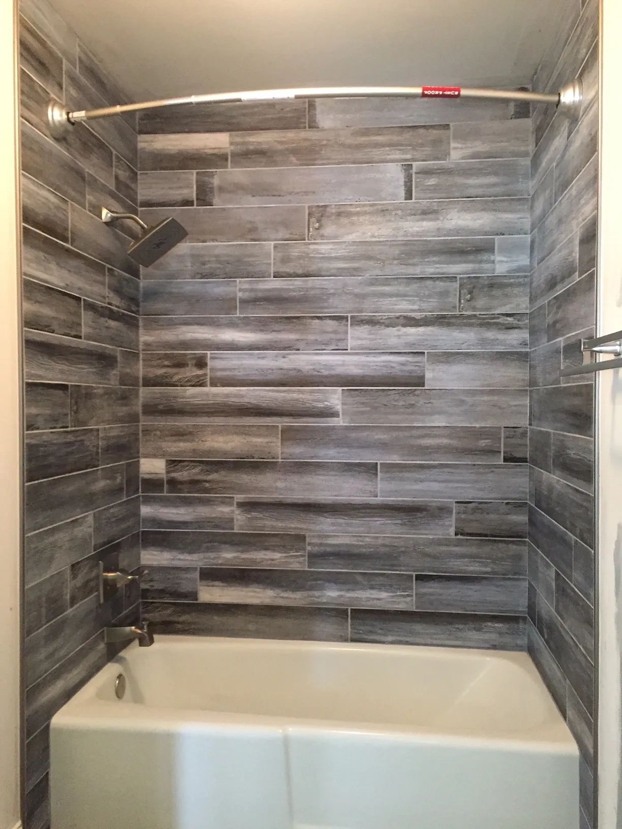 Bathroom tub with gray wood-look tile shower walls and updated fixtures in a Kansas City remodel