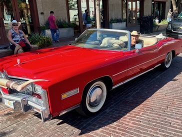 A bright red vintage convertible with a driver in a cowboy hat.